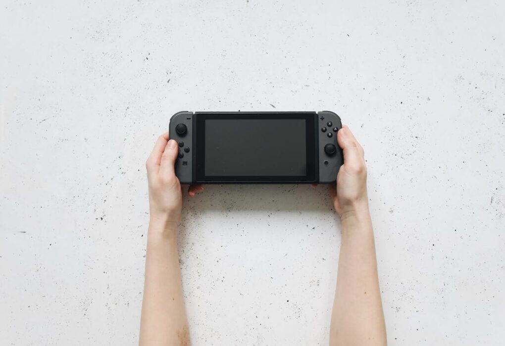 Una persona sostiene una consola Nintendo Switch 2 en sus manos sobre una mesa blanca Source: https://www.pexels.com/photo/hands-holding-nintendo-switch-near-white-surface-4523008/