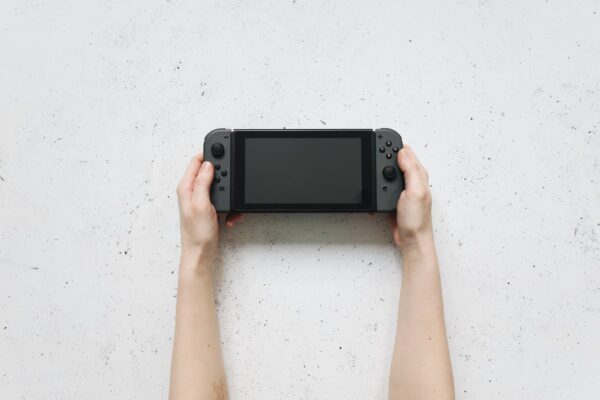 Una persona sostiene una consola Nintendo Switch 2 en sus manos sobre una mesa blanca Source: https://www.pexels.com/photo/hands-holding-nintendo-switch-near-white-surface-4523008/