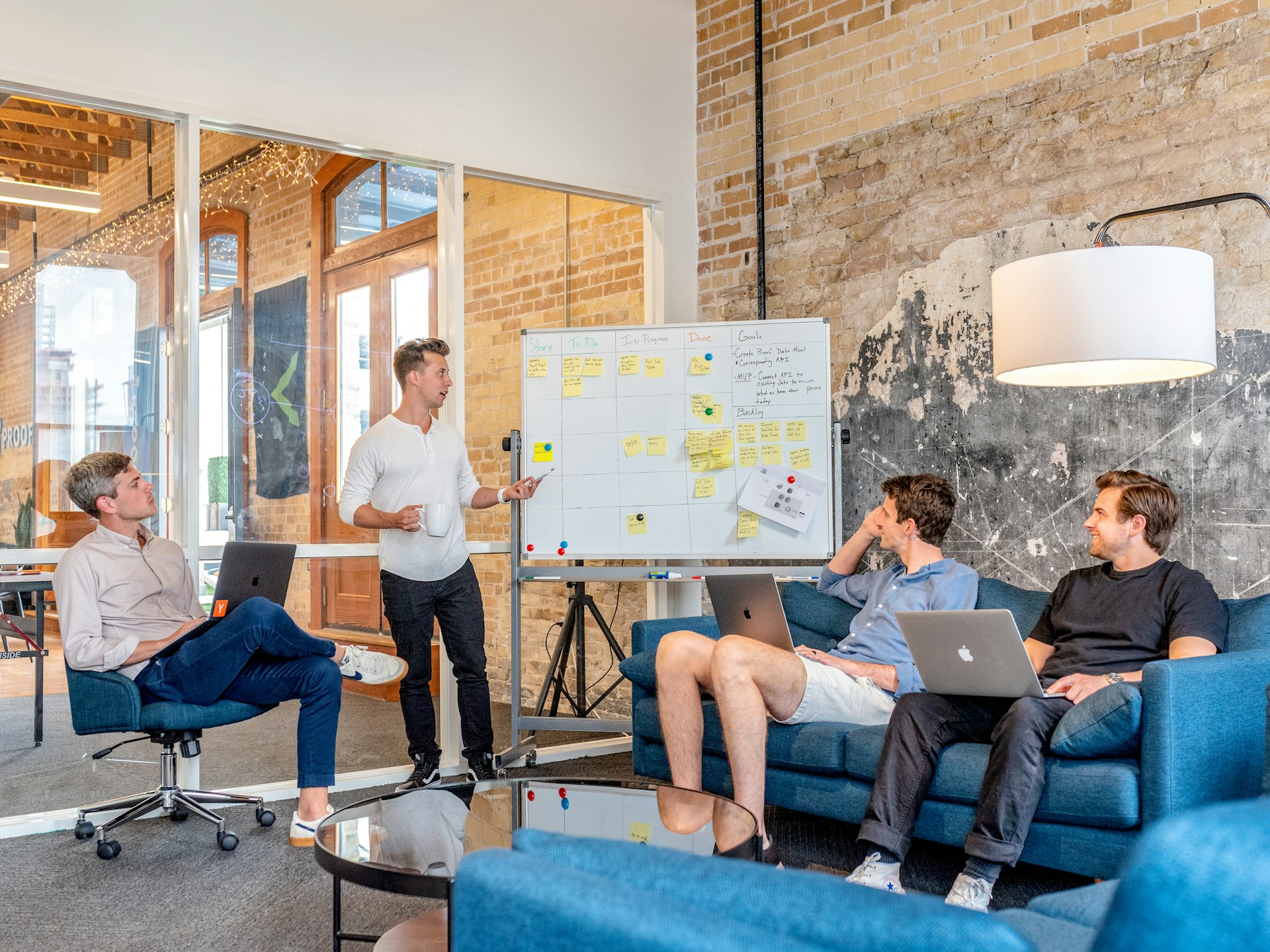 Un grupo de empleados discutiendo las mejores formas de posicionar su marca en una oficina moderna. fuente de imagen: https://unsplash.com/photos/three-men-sitting-while-using-laptops-and-watching-man-beside-whiteboard-wD1LRb9OeEo