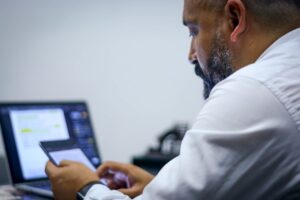 Un hombre de negocios sentado en su escritorio, mirando una tableta con una computadora portátil frente a él para representar las tendencias digitales en Ecuador.